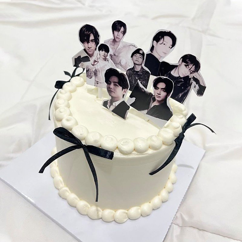 Minimalist white cream BTS theme birthday cake with black ribbon bows and member photo toppers, customized cake Karachi.